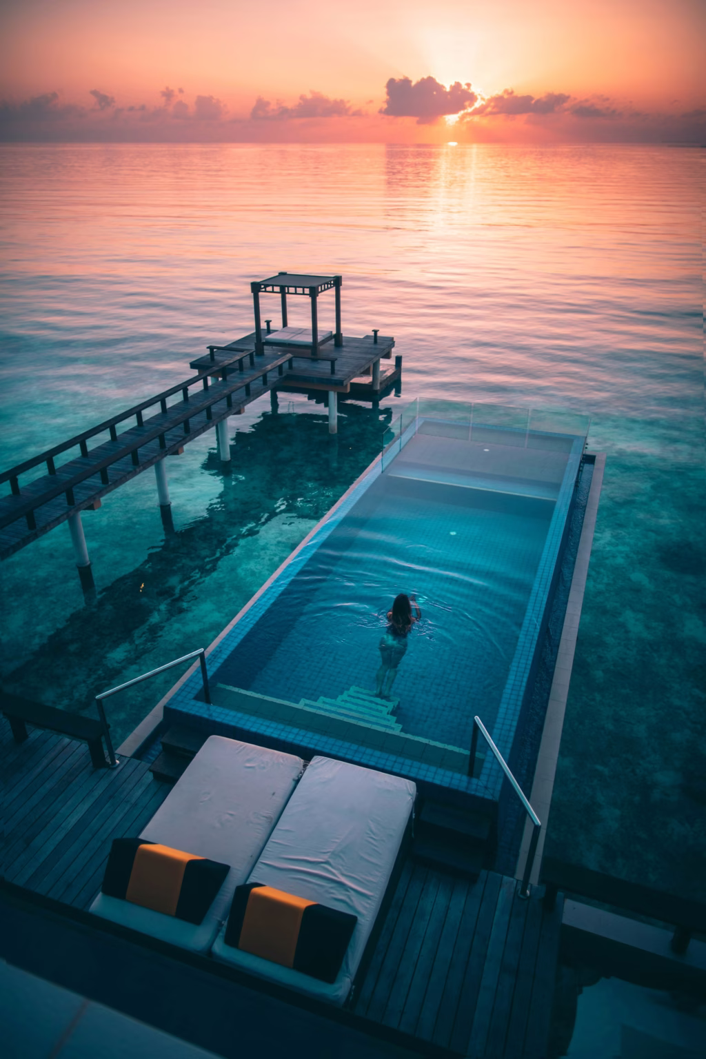 Swimmer in an infinity pool over the lagoon at sunrise